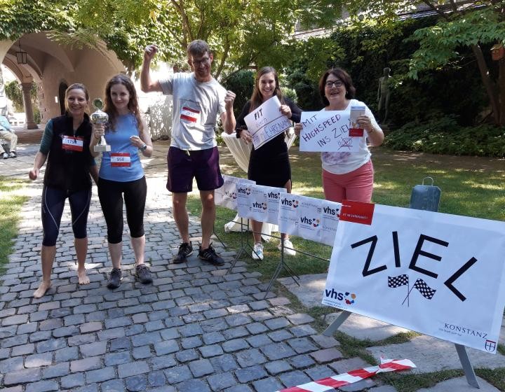 fünf Personen in Sportkleidung stehen nebeneinander vor einer rot-weiß markierten Ziellinie