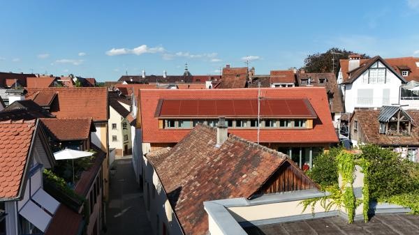 Dachlandschaft einer historischen Altstadt. In der Mitte ein rotes Dach, das mit roten Solar-Paneelen belegt ist