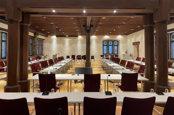 Blick in den Konstanzer Ratssaal mit im Rechteck aufgestellten Tischen und roten Stühlen