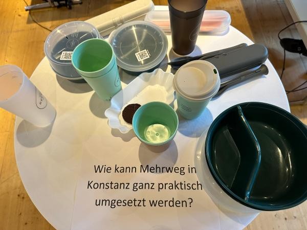 Blick auf einen weißen runden Bistrotisch, auf dem mehrere Mehrwegbecher und -schalen stehen
