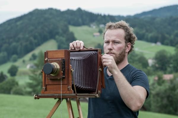 Mann mit historischer Kamera in grüner Landschaft