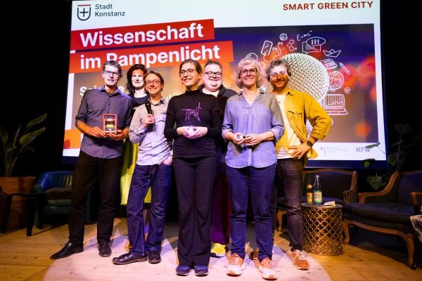 Gruppenfoto der SlamerInnen auf der Bühne. Im Hintergrund ist die Präsentation „Wissen-schaft im Rampenlicht, Science Slam zur Stadt der Zukunft von Smart Green City, Stadt Konstanz“ zu sehen.