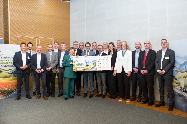 Mehrere Personen im Innenraum. Sie halten ein großes Banner mit verschiedenen Logos