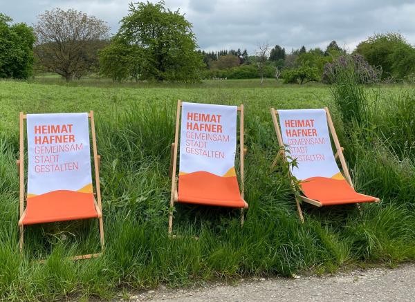 Drei Orange-weiße Liegestühle stehen auf einer grünen Wiese.