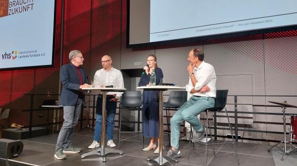 Vier Personen während einer Diskussionsrunde an zwei runden Stehtischen