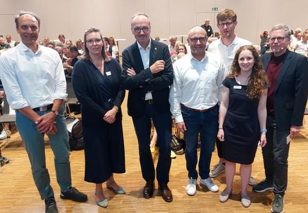 Siebenköpfige Personengruppe posiert nebeneinander stehend für ein Foto